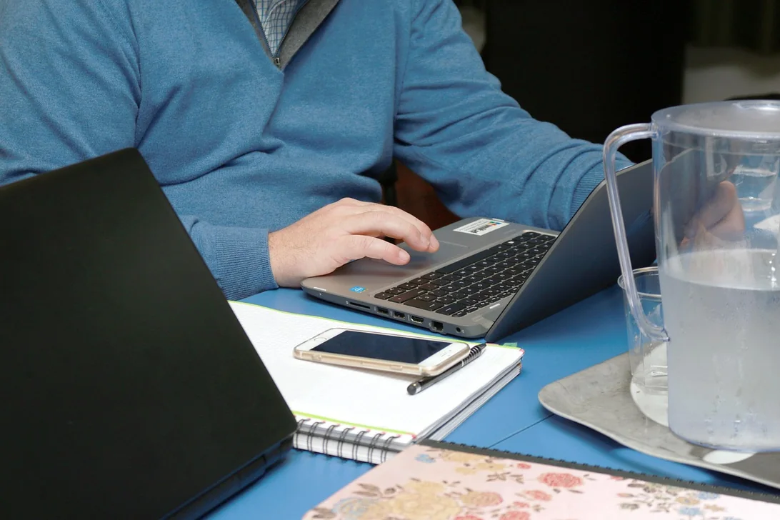 Personne travaillant sur un ordinateur portable, carnet et téléphone posés sur la table